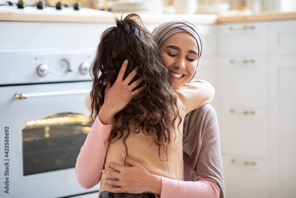 Mother's Day. Loving Little Girl Hugging Islamic Mommy In Kitchen At Home Mother's Day. Loving Little Girl Hugging Islamic Mommy In Kitchen At Home