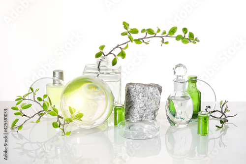 Natural Green laboratory. Abstract floral arrangement. Grey granite podium with product in transparent glass vial. Reflections of leaves distorted in water. Springtime green twigs in jars, tubes.