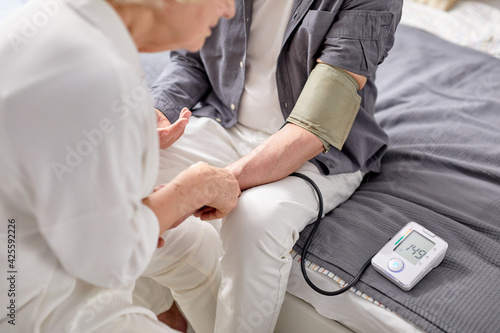 Blood pressure. Gray-haired elderly woman helping her sick husband to check blood pressure
