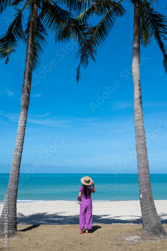 A woman standing with her back on the beach with a coconut tree at Samila beach, Songkhla, Thailand © Krisda