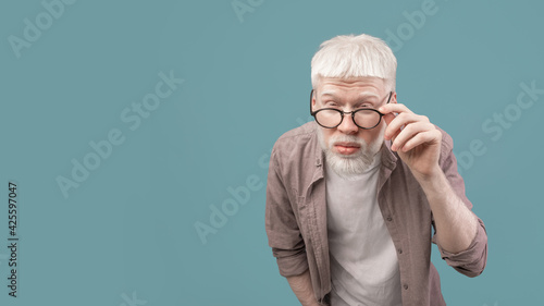 Vision problems. Young albino guy in eyeglasses squinting eyes, blue background, panorama with free space