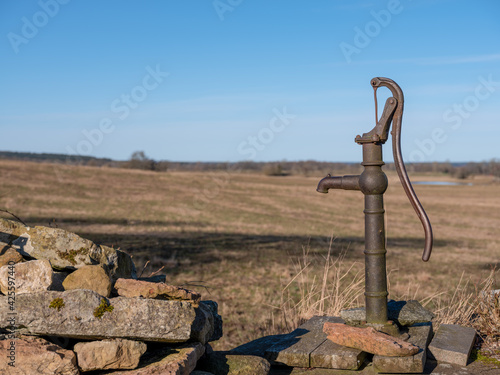 Fotografia, Obraz Old water pump with handle by a well in rural farmland