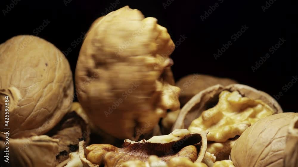 A broken walnut in half on a black background, in a heap with other nuts spins and stops quickly. Close-up. A broken walnut in half on a black background, in a heap with other nuts spins and stops quickly. Close-up.