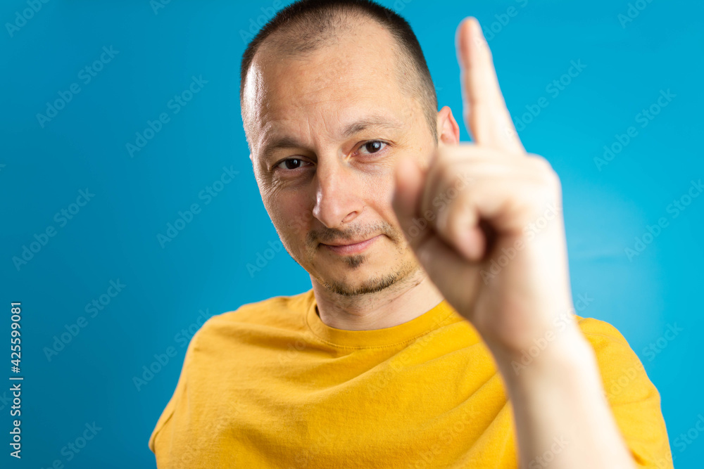 Attractive middle aged man in yellow t-shirt pointing up with his finger isolated on blue background. Attractive middle aged man in yellow t-shirt pointing up with his finger isolated on blue background.
