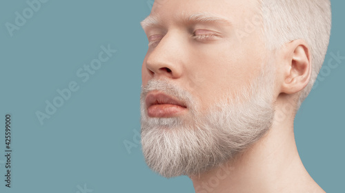 фотографія Calm bearded albino man with closed eyes resting against turquoise background, p
