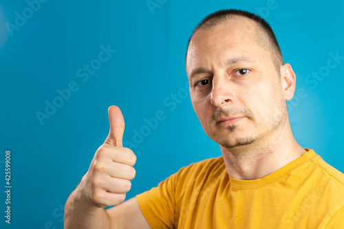 optimistic man isolated on blue background showing thump up with positive emotions of content and happiness. 