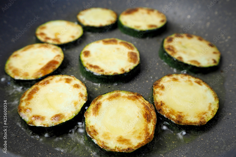 the process of frying green sliced zucchini slices in a gray pan side view . vegetarianism