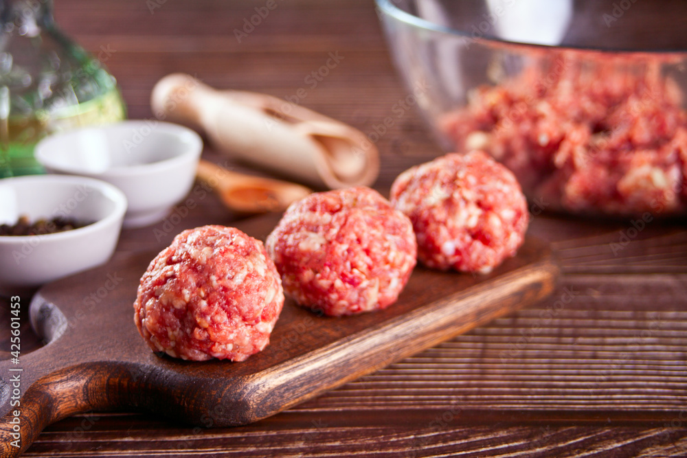 Raw meatballs on the wooden cutboard with ingredients on the background