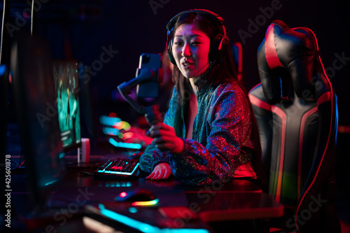 A young beautiful asian girl is broadcasting online on a smartphone with the help of a three-axis stabilizer. Female gamer at the esports tournament.
