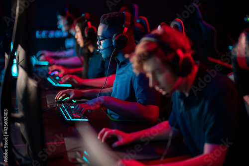 A multi-racial team of esports athletes conducts a training session before an online shooter tournament. Neon light. photo