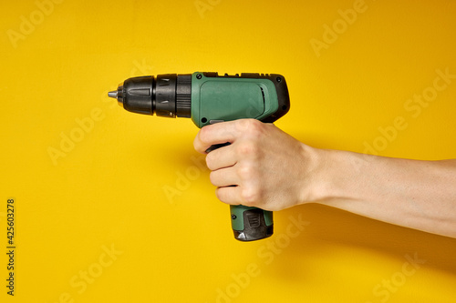 Green cordless battery powered drill on yellow background