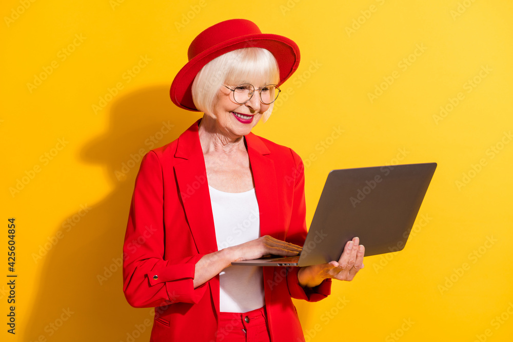 Photo portrait of senior business woman working on laptop in glasses red formal wear isolated vivid yellow color background Photo portrait of senior business woman working on laptop in glasses red formal wear isolated vivid yellow color background