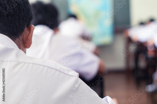 Back of students taking exam and writing answer in classroom with stress