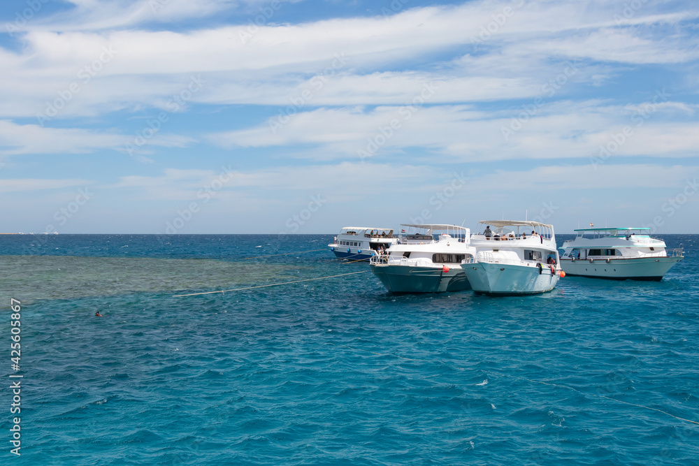 Panoramic view of the Red Sea, coral reef and moored pleasure boats. Blue and white seascape, white boats and clear blue water with cloudy blue skies