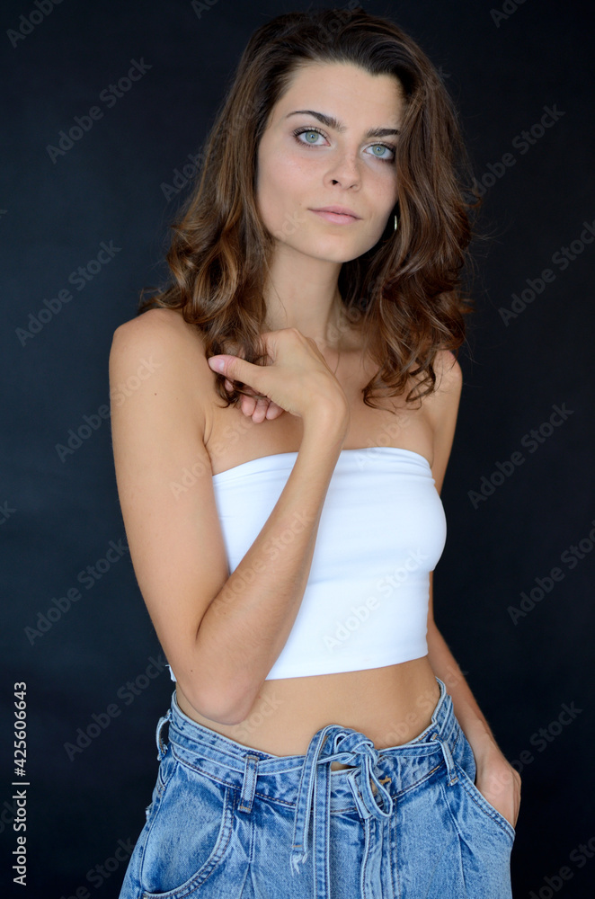 Young Polish woman in studio with black background. Slim woman with dark hairs, wearing white top and blue jeans. Young Polish woman in studio with black background. Slim woman with dark hairs, wearing white top and blue jeans.