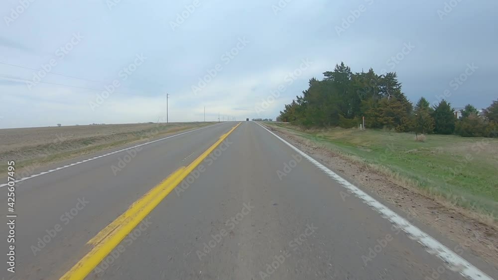 Point of view driving on a straight stretch of country highway, past a farm yard and harvested fields; rural south central Nebraska on a cloudy winter day Point of view driving on a straight stretch of country highway, past a farm yard and harvested fields; rural south central Nebraska on a cloudy winter day