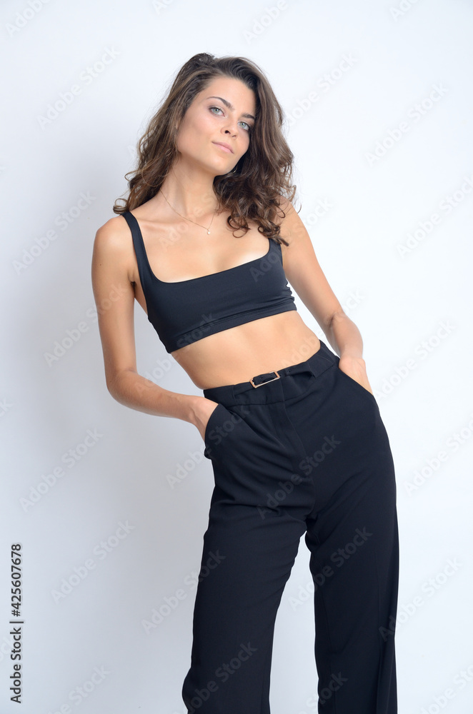 Naklejka premium Young Polish woman in studio. Slim woman with dark hairs wearing black top and black trousers.