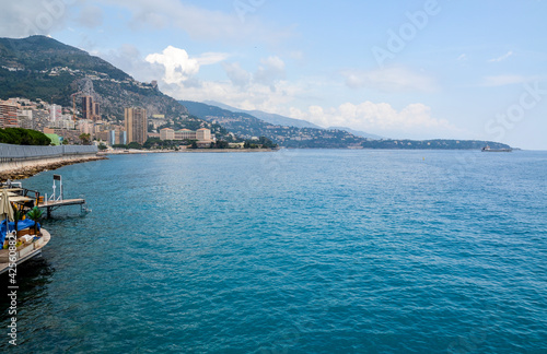 City of Monaco coastline Mediterranean Sea beach residential buildings against high mountains day time blue sky and clouds on seascape background 