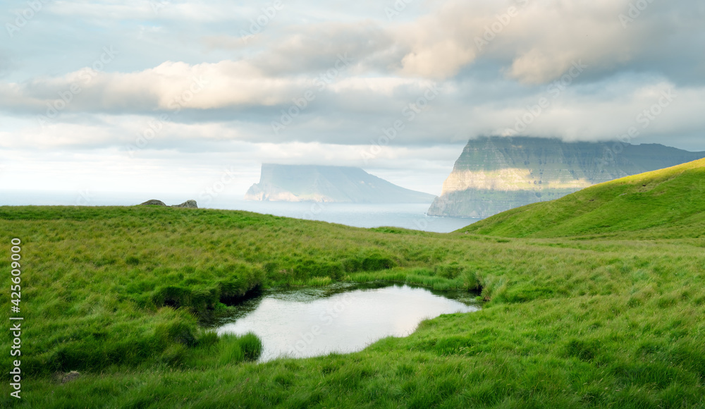 Lonely tourist near small lake looks at foggy islands in Atlantic ocean