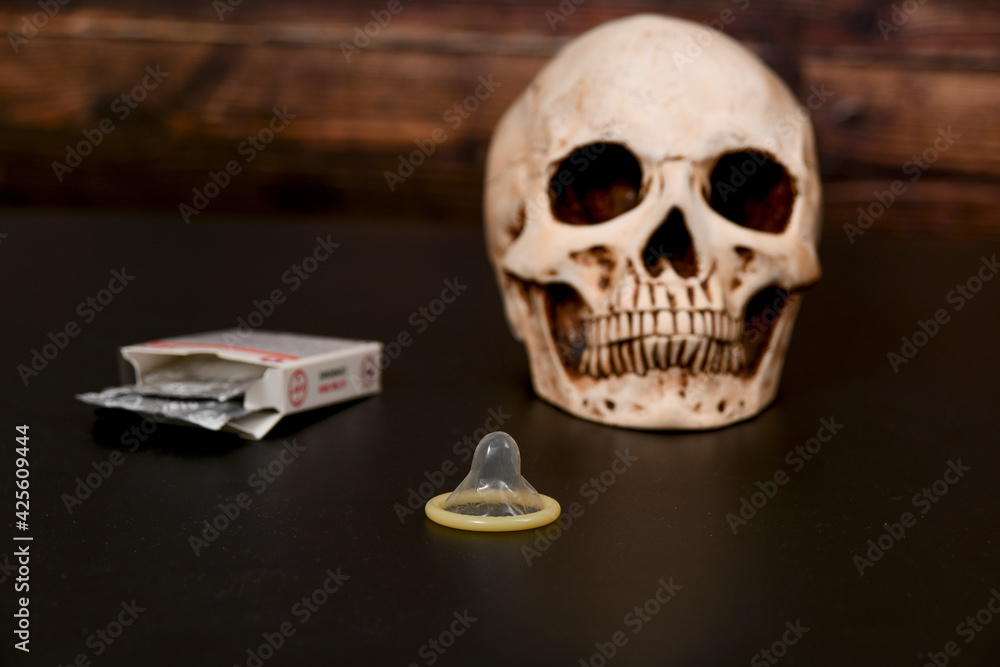 Opened condom near the skull on a dark background. Pregnancy, abortion and death concept. Opened condom near the skull on a dark background. Pregnancy, abortion and death concept.