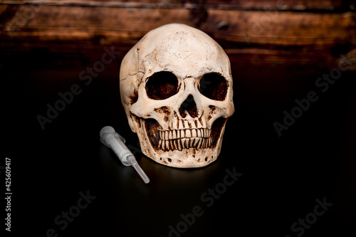 Skull and syringe on a dark wooden background.