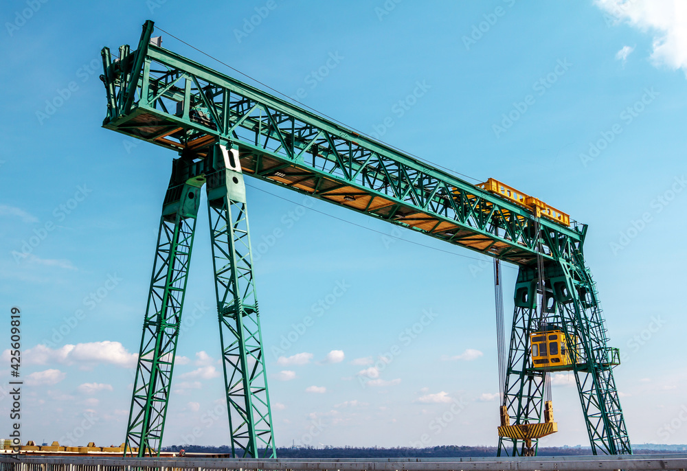 Green gantry bridge crane at work over blue sky