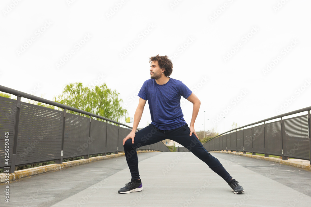 a young male athlete trains on the street by stretching his legs