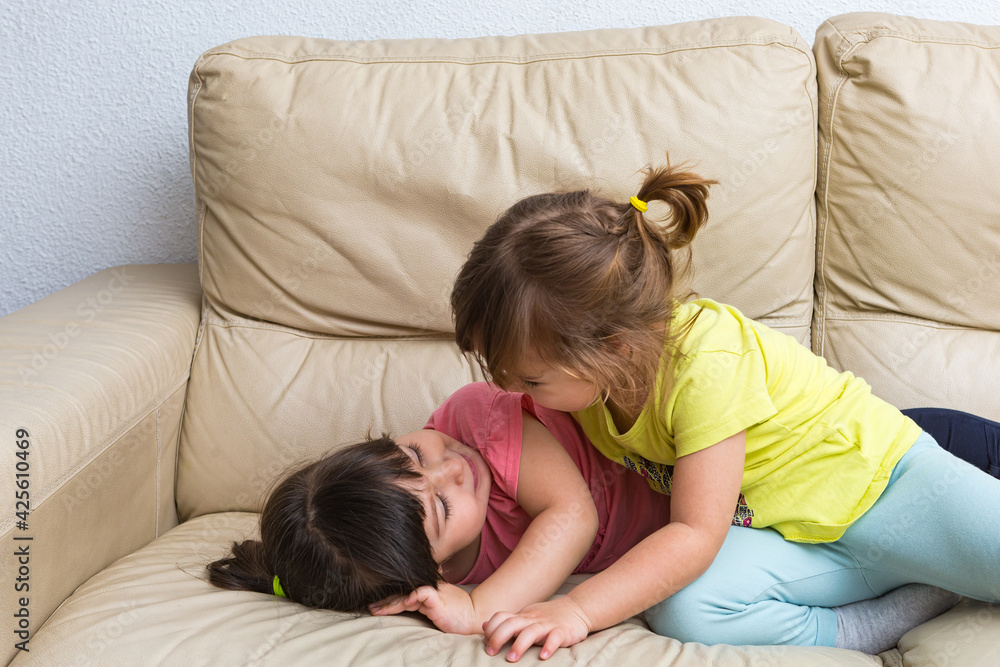 Two girls sister embraced, lying on a sofa playing Two girls sister embraced, lying on a sofa playing