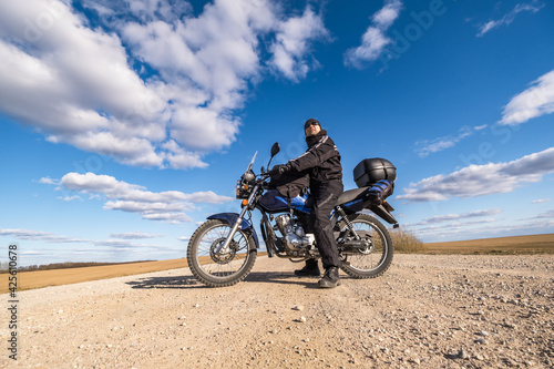  man in a black uniform on bike against the backdrop of panorama of field and blue sky. motorcycle travel concept © hiv360