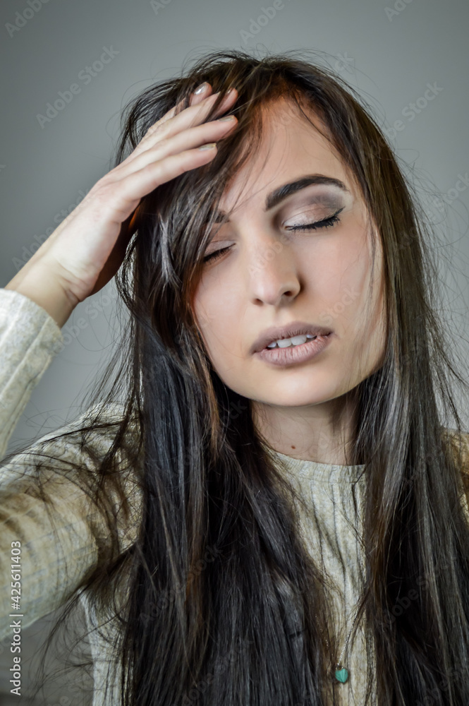 Fototapeta premium Portrait of a beautiful young woman with long brown hair suffering from headache and touching her forehead
