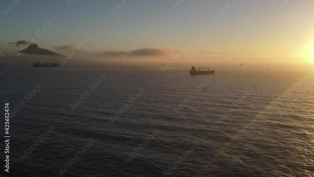 Drone shot over the ocean at sunset of mountains in clouds and container ship. Drone shot over the ocean at sunset of mountains in clouds and container ship.