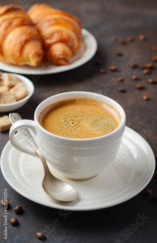 Cup of fresh coffee with croissants on dark background.