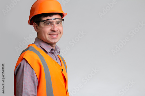 Young construction worker in hard hat and reflective vest on grey studio background