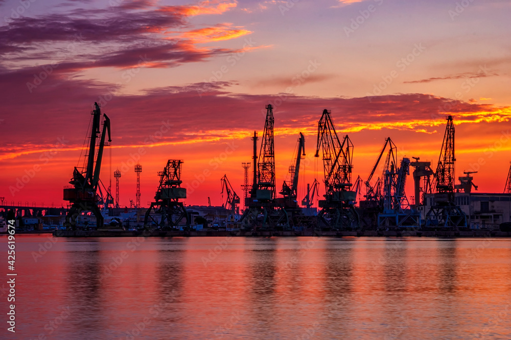 Silhouettes of port cranes at stunning red sunset. Cargo ship terminal at the twilight scene.