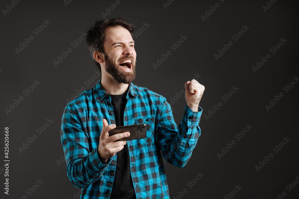 Fototapeta premium Excited man making winner gesture while playing online game on cellphone