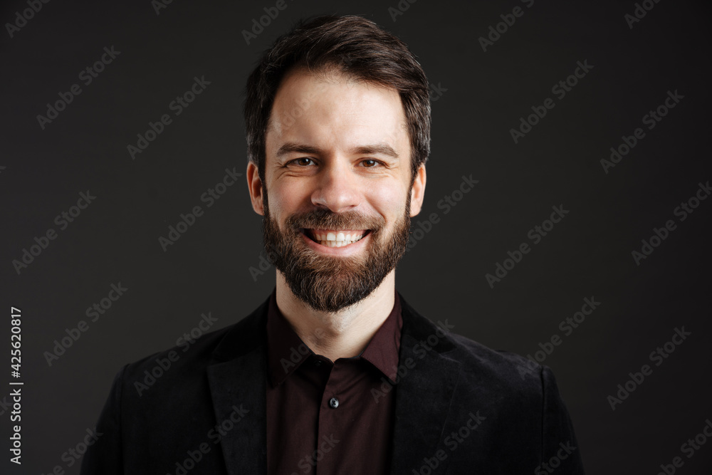 Fototapeta premium Bearded happy man in black jacket smiling and looking at camera