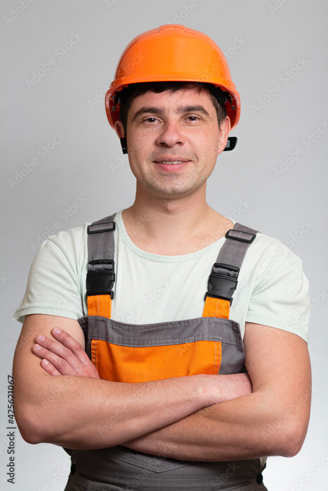 confident young construction worker in hard hat and overalls with arms folded on the chest on grey studio background confident young construction worker in hard hat and overalls with arms folded on the chest on grey studio background