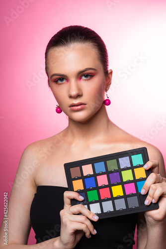 Beautiful woman in round pink earrings holds a colorchecker in hands