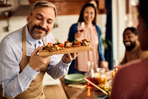 Fotografi Happy man serving appetizer to his friends during lunch time at home