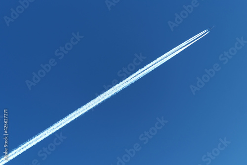 Vierstrahliges Flugzeug mit weißen Kondensstreifen als Diagonale und blauer Himmel - Stockfoto