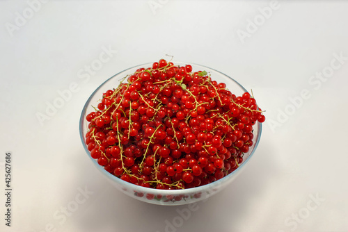 Large bowl of red currant with sprigs on a white background.