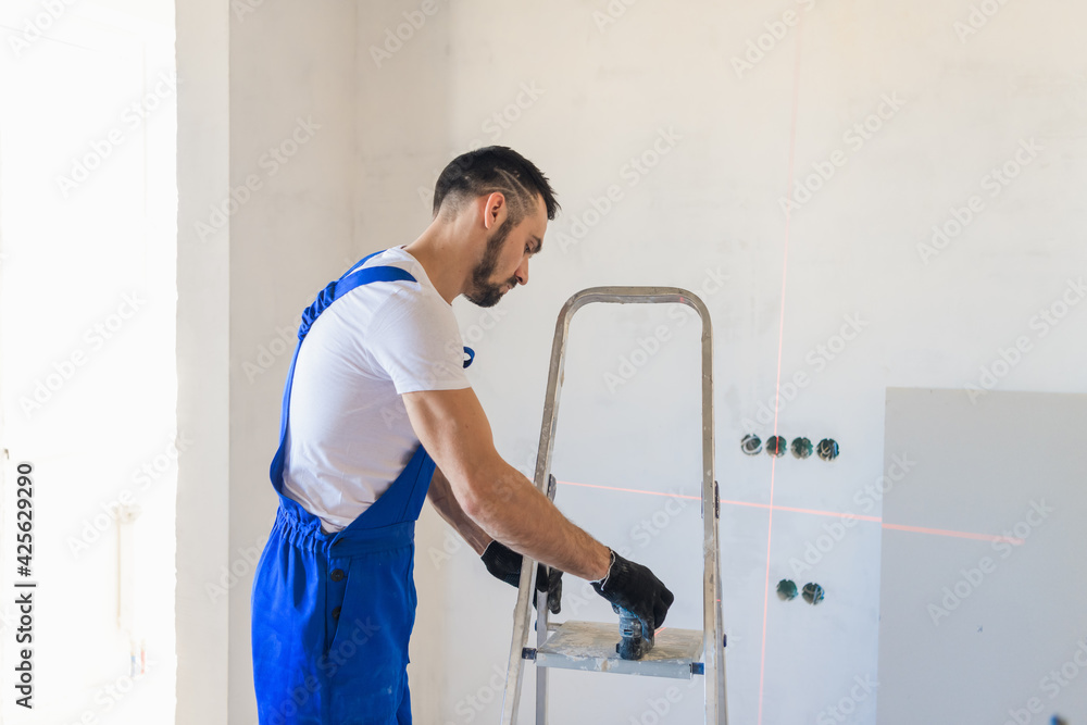 The worker uses a stepladder and a laser level The worker uses a stepladder and a laser level