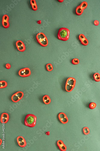 Beautiful pattern made of fresh red chili peppers cut into thin slices on a dark green background. Flat lay creative arrangement. photo