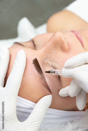 Kosmetyczka robi makijaż permanentny brwi, tatuaż na twarzy kobiety. Zbliżenie na proces pigmentacji brwi. 