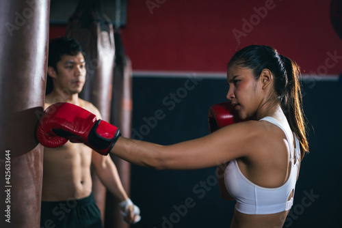 Young Asian doing boxing or Muay Thai punching sandbag instructor by male trainer in fitness club or gym. healthcare and sport concept. © structuresxx