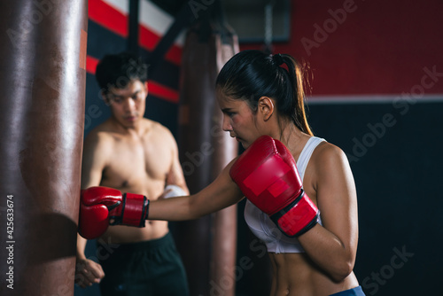 Young Asian doing boxing or Muay Thai punching sandbag instructor by male trainer in fitness club or gym. healthcare and sport concept.