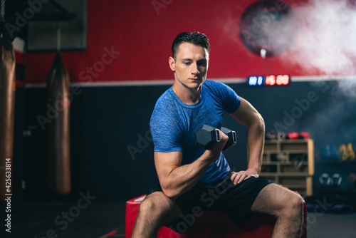 Sporty Caucasian man lifting dumbbell training for maintain muscle in fitness club or gym.