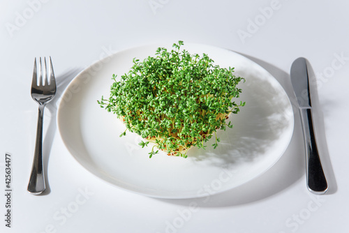 Obraz na płótnie Fresh sprouts of cress on white plate and cutlery on sides on white background. Growing microgreens at home. Healthy eating concept. w salonie
