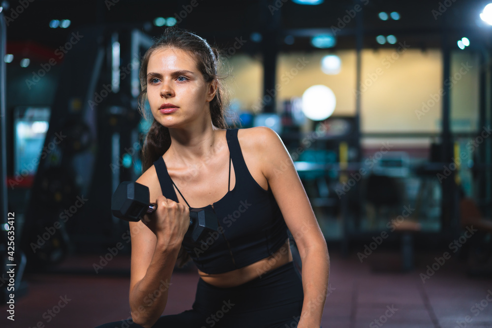 Caucasian young woman in sportswear lifting dumbbell  in fitness club or gym.