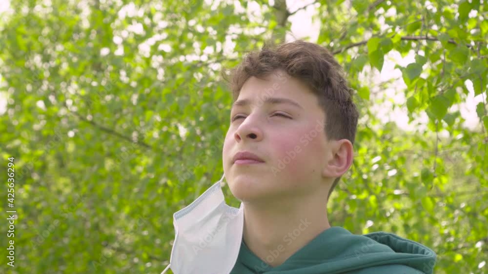 Teenager takes off his medical protective mask and takes a deep breath of fresh air in the forest against the backdrop of lush foliage of spring trees. Close-up portrait Teenager takes off his medical protective mask and takes a deep breath of fresh air in the forest against the backdrop of lush foliage of spring trees. Close-up portrait